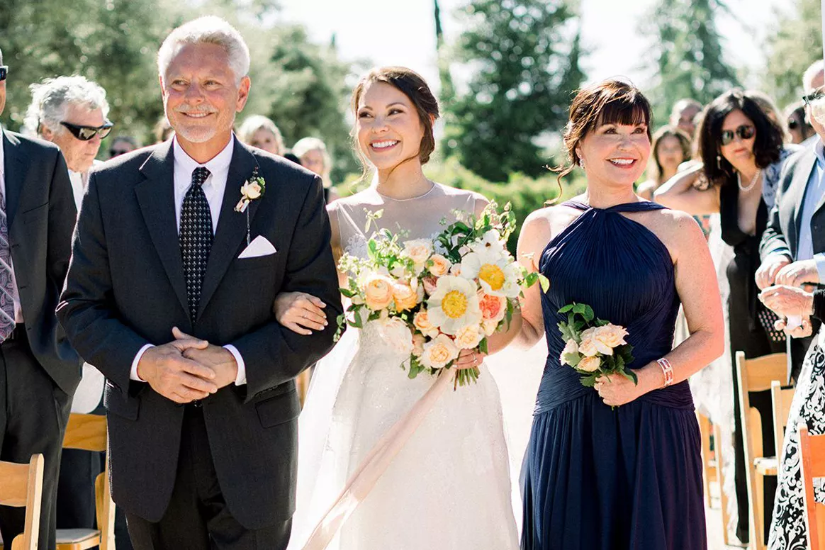 bride and parents walk down aisle outdoors